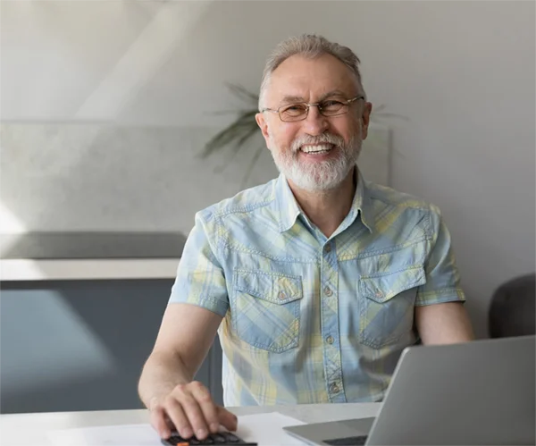 Happy Man sitting at desk with open computer wearing glasses